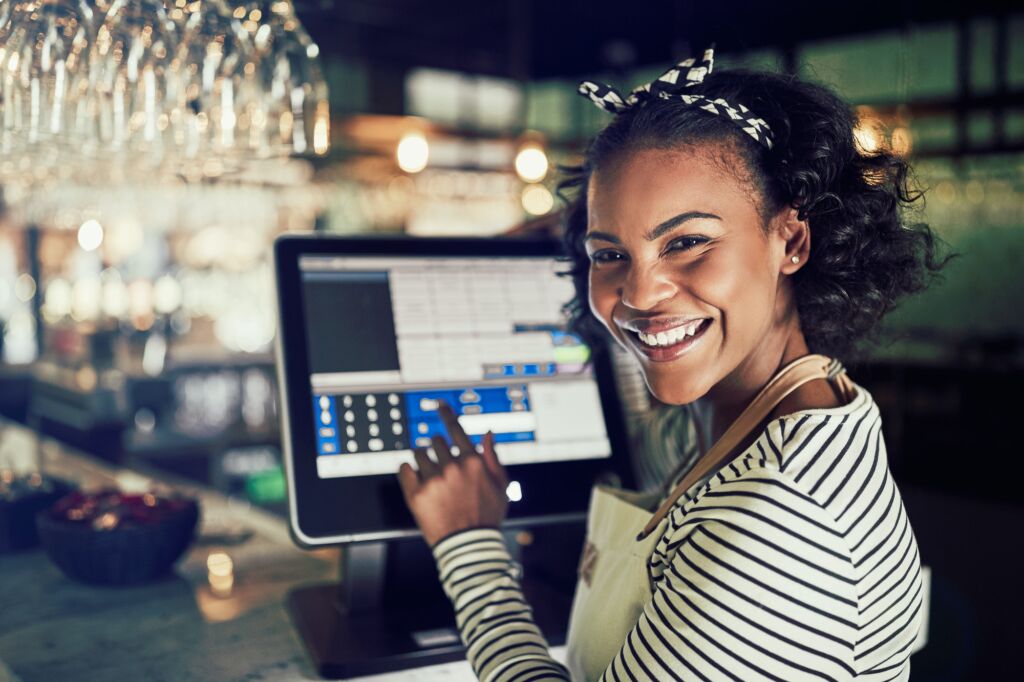 Smiling African waitress using a restaurant point of sale terminal